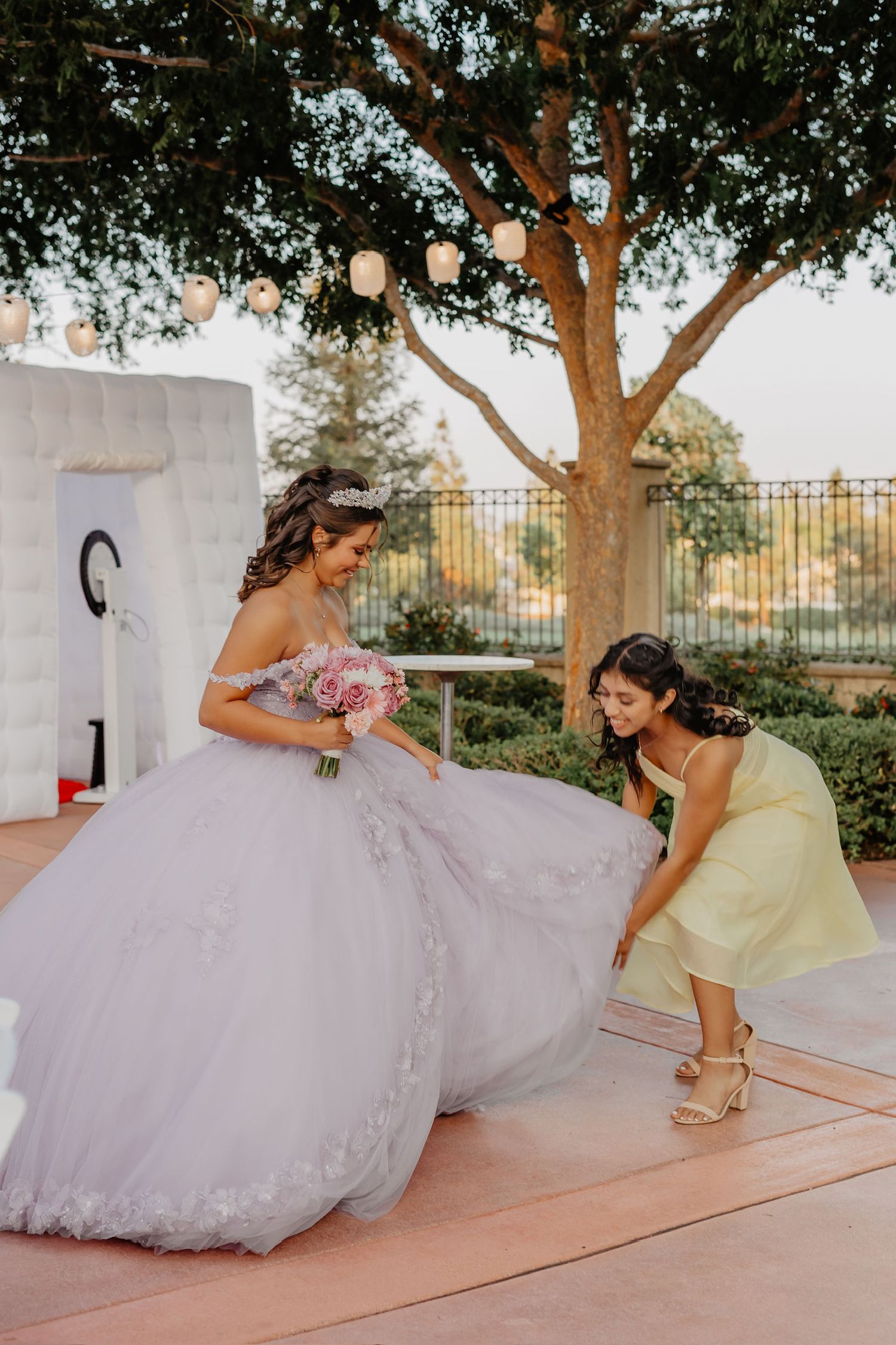 A bride in a flowing ballgown twirls gracefully on a patio while a young attendant in yellow watches with delight.