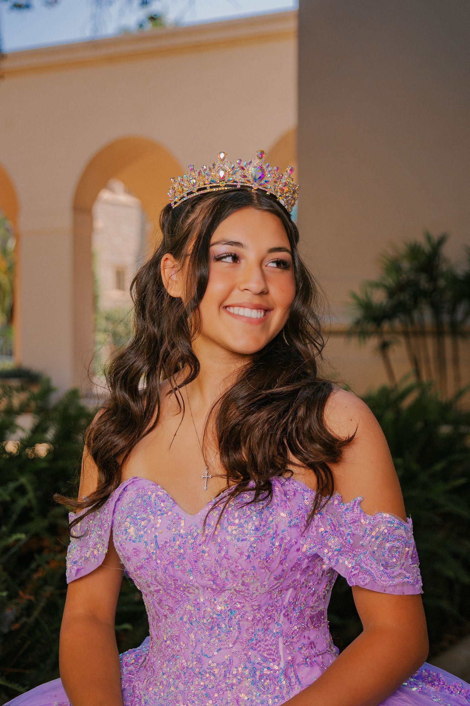 A person in a sparkly purple off-shoulder gown and tiara smiles in a series of outdoor portrait photos.