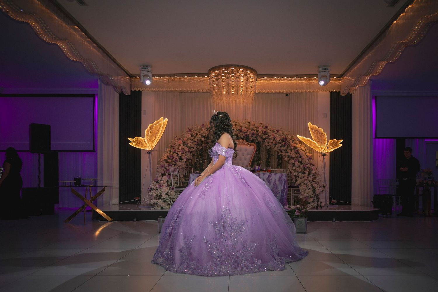 A lavender ballgown dress illuminated by purple lighting on an empty dance floor creates a magical atmosphere.
