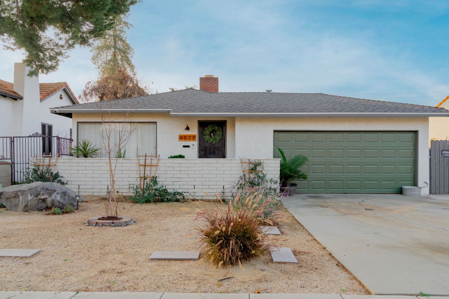 Single story ranch home with green garage door and desert landscaping in front yard under blue sky.