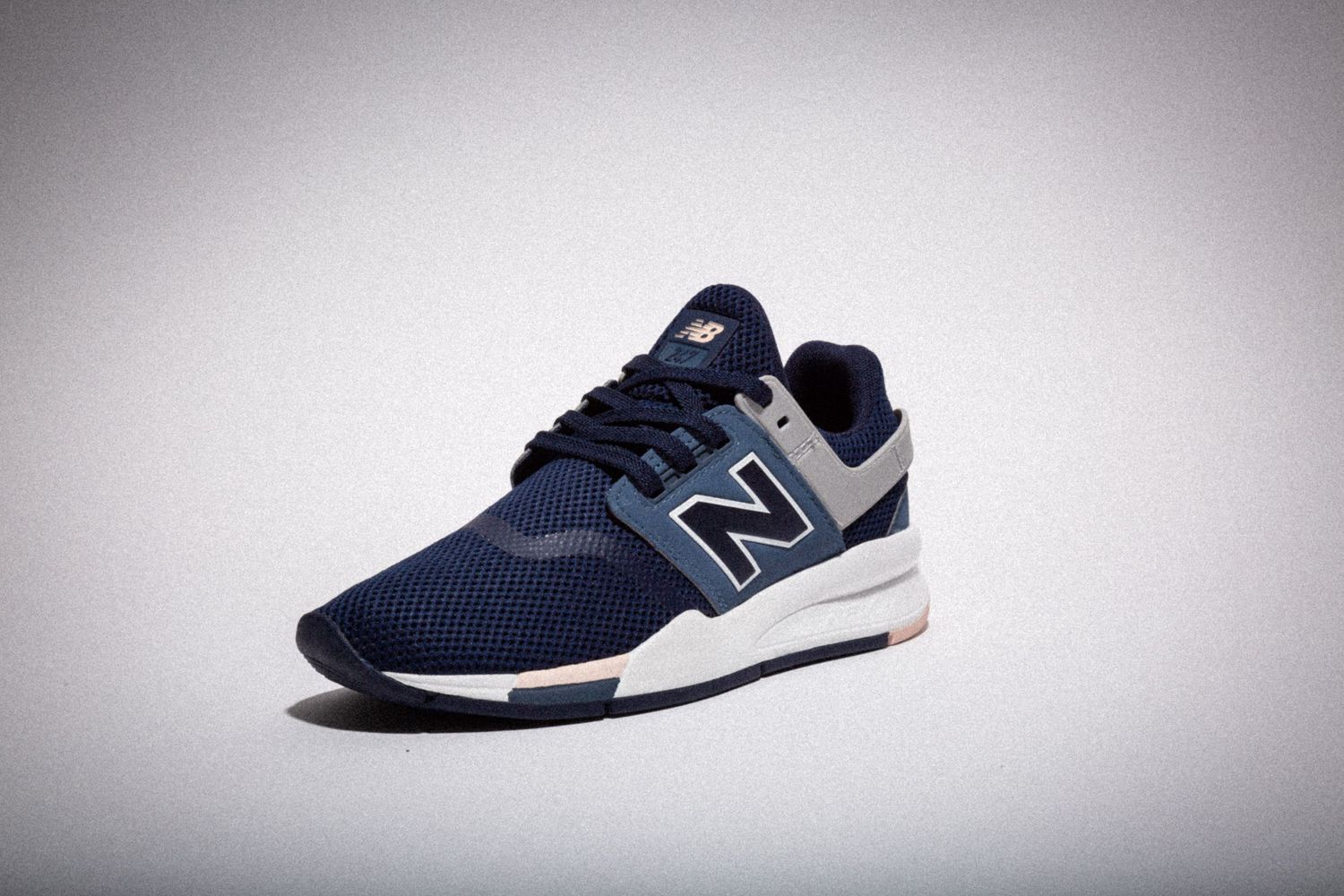 New Balance athletic sneaker in navy blue with white sole shown from multiple angles on gray background.