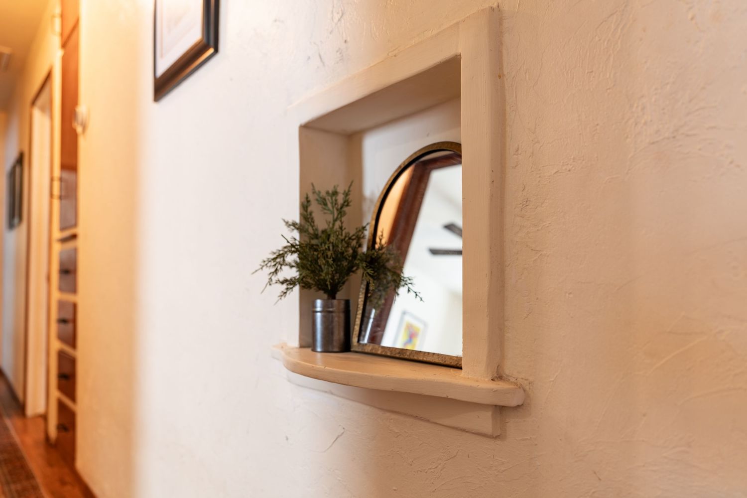 Narrow hallway with beige walls features modern wall sconces and decorative mirrors creating a bright welcoming space.