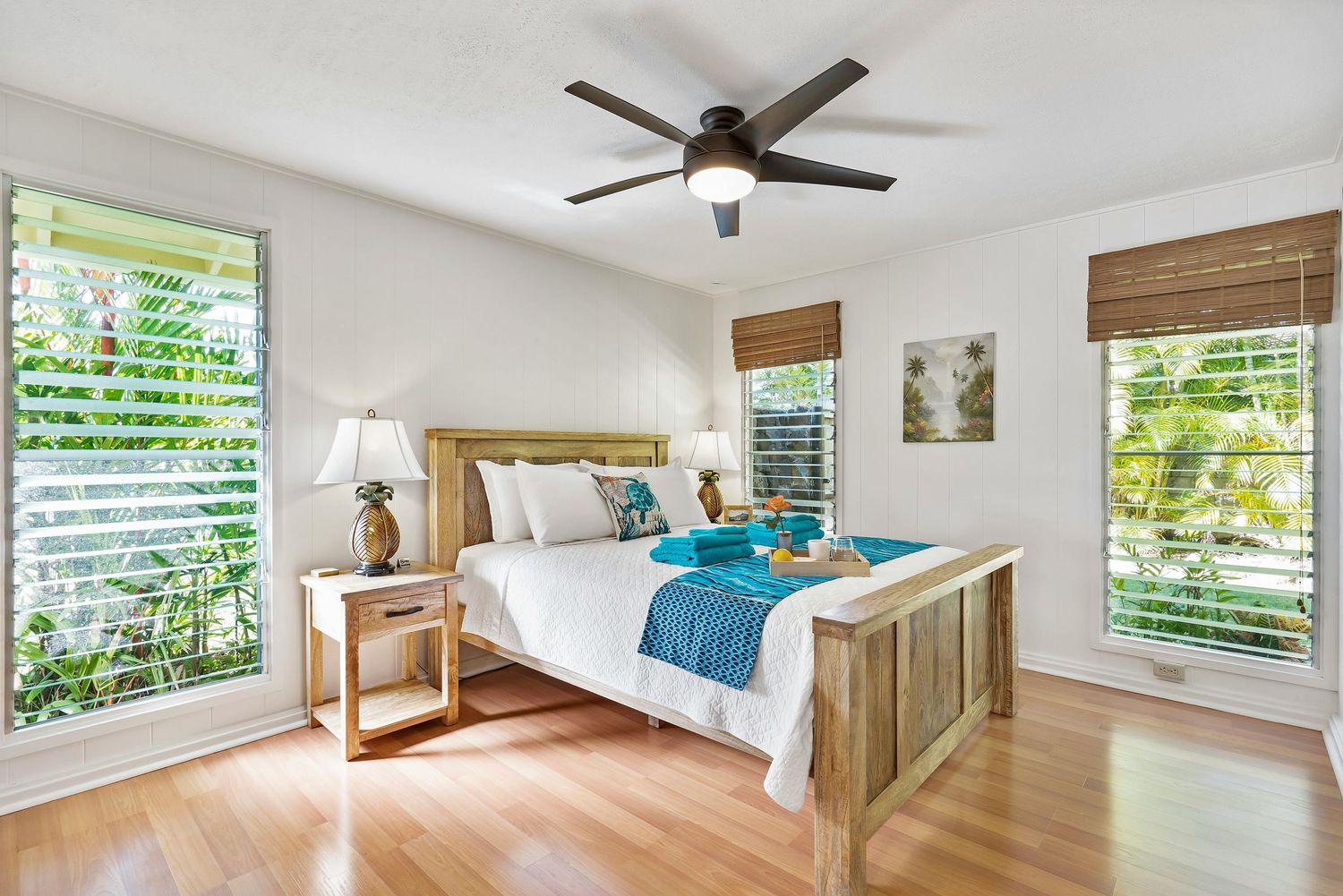 Bright modern bedroom with white walls, bamboo shades, and tropical views through multiple windows.