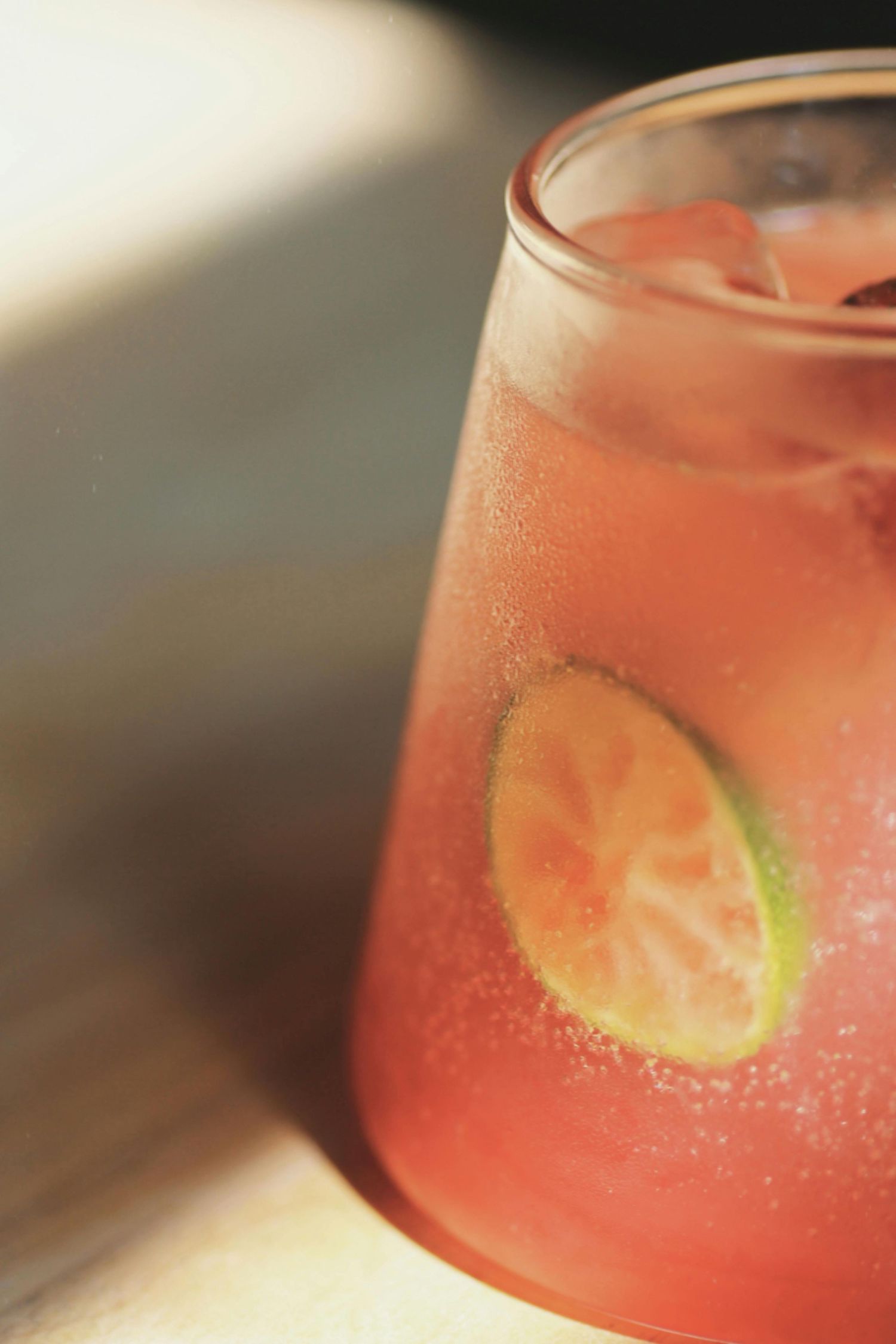 A vibrant pink cocktail garnished with a lime wedge in a clear glass with condensation on the surface.