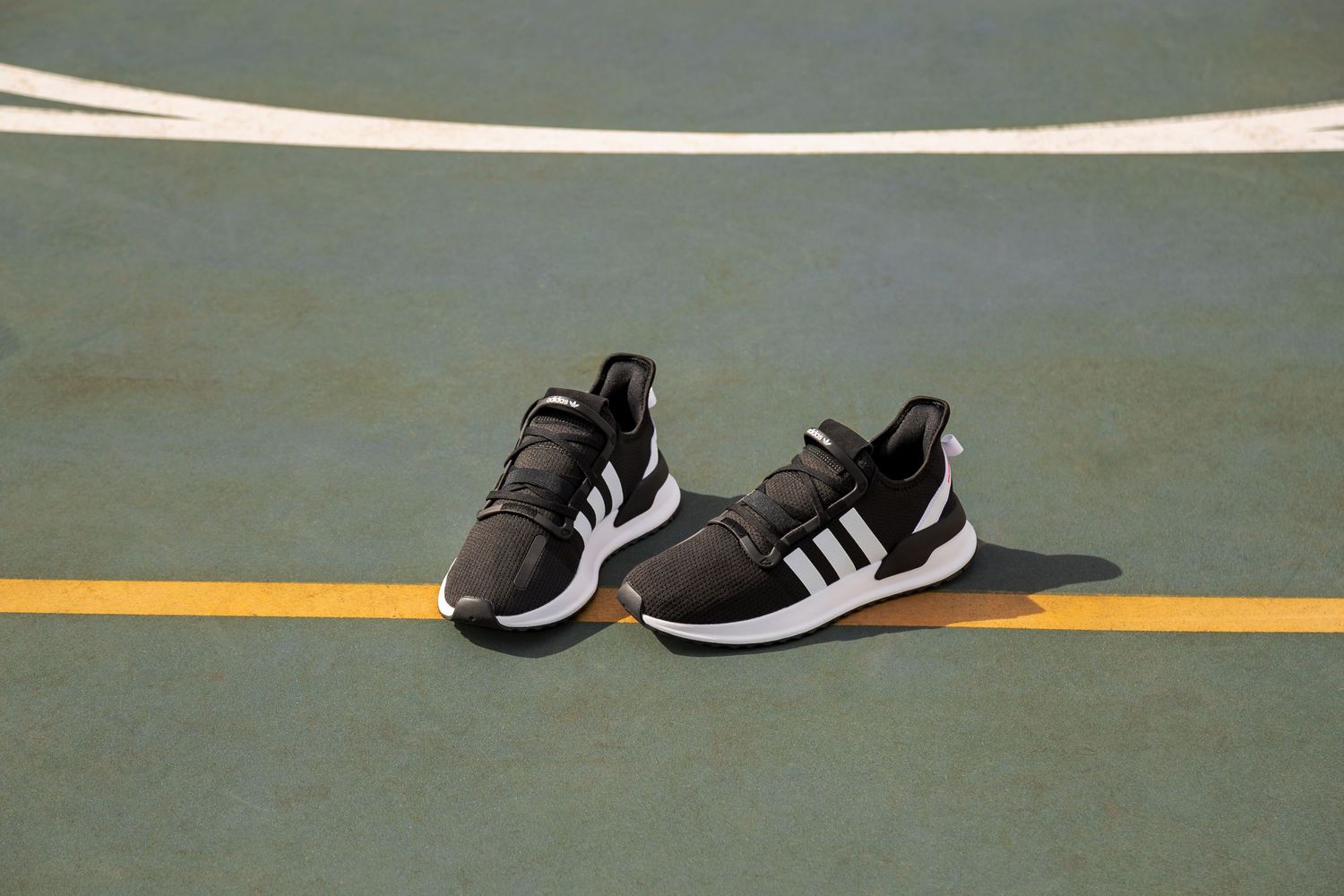 Black and white athletic sneakers lined up on a green floor with yellow lines.