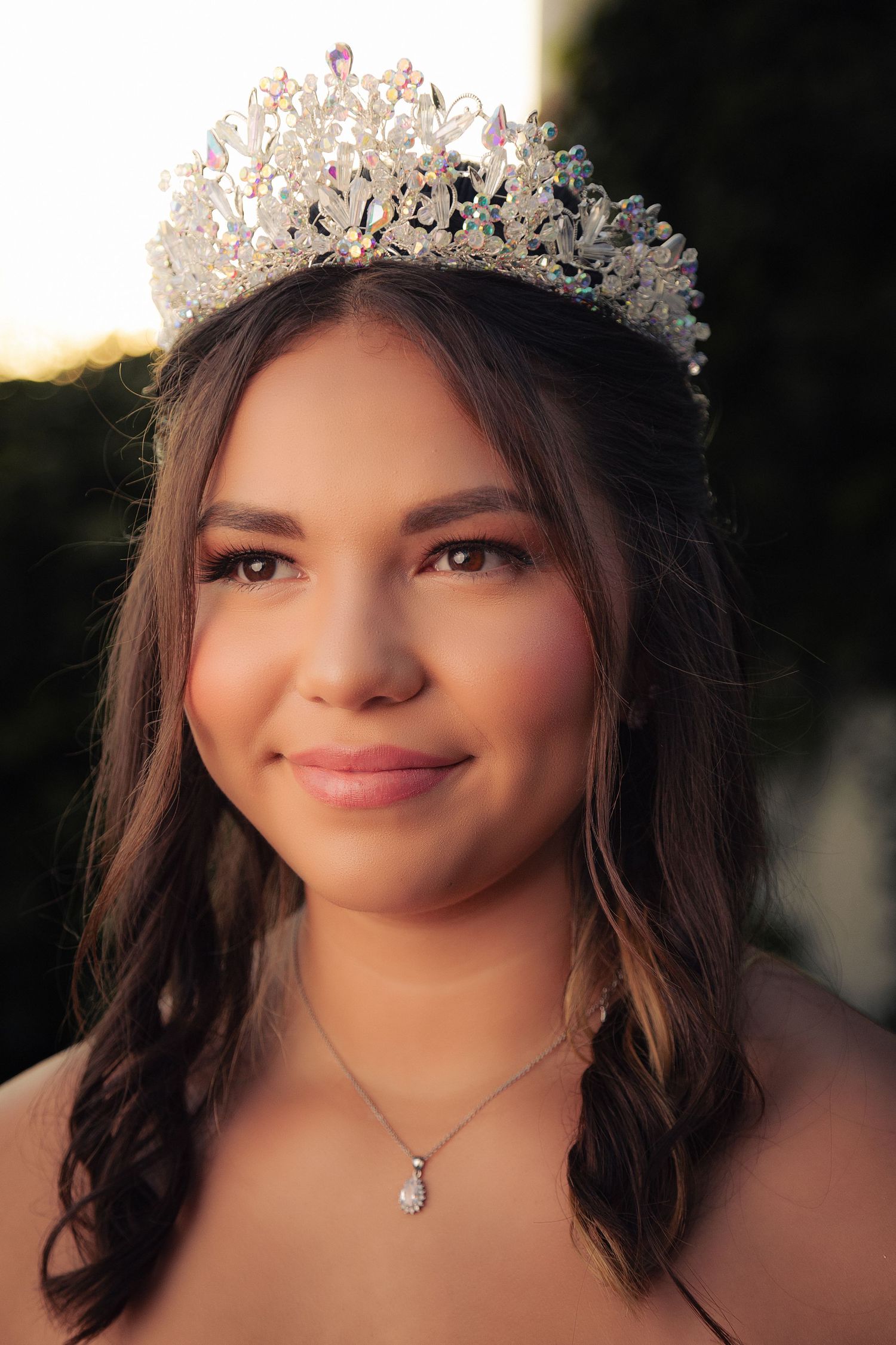 A close-up portrait shows someone wearing a delicate crystal crown and teardrop necklace in warm sunset lighting.