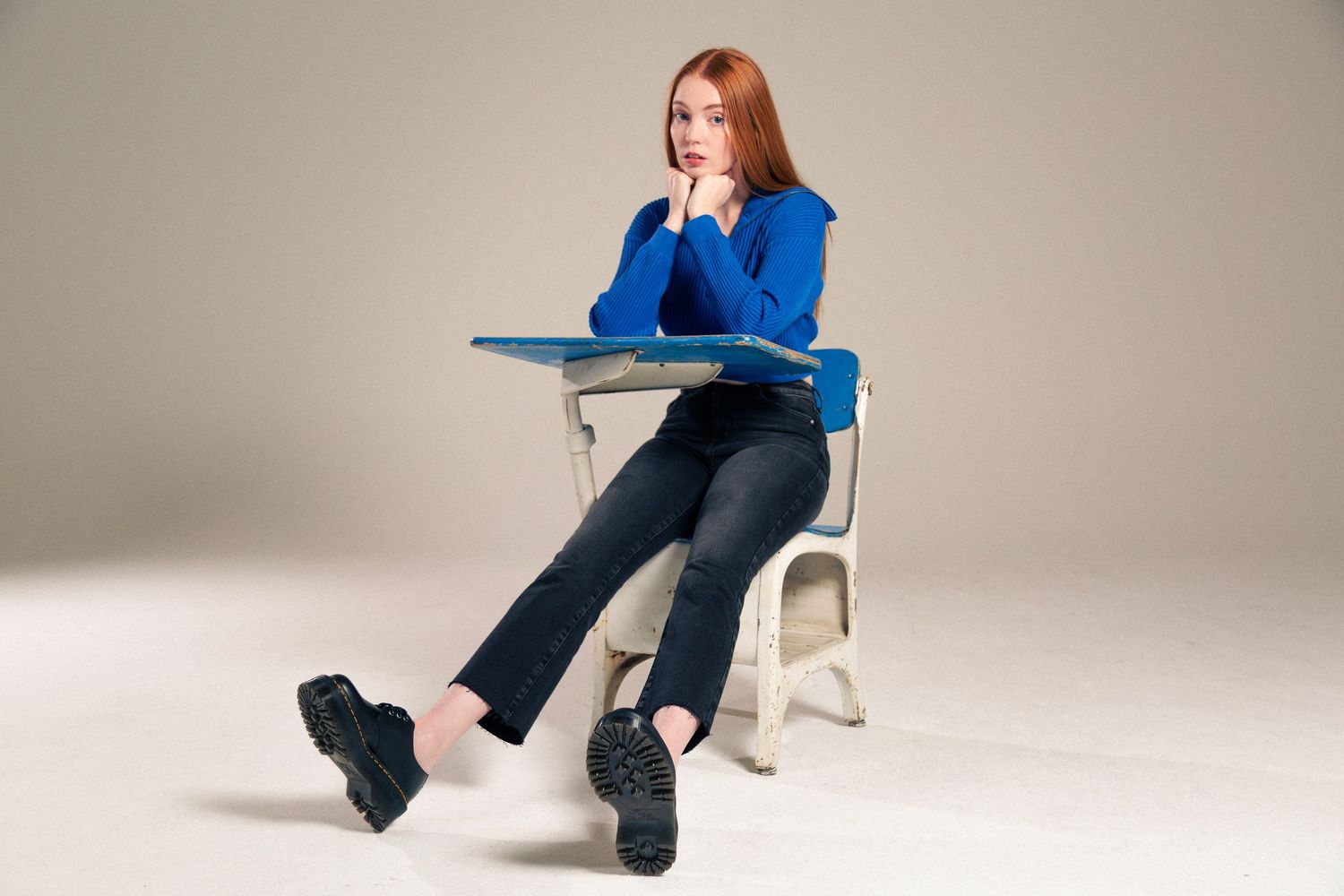 Model in a bright blue blazer and dark pants sits in various poses on a white chair against a neutral backdrop.