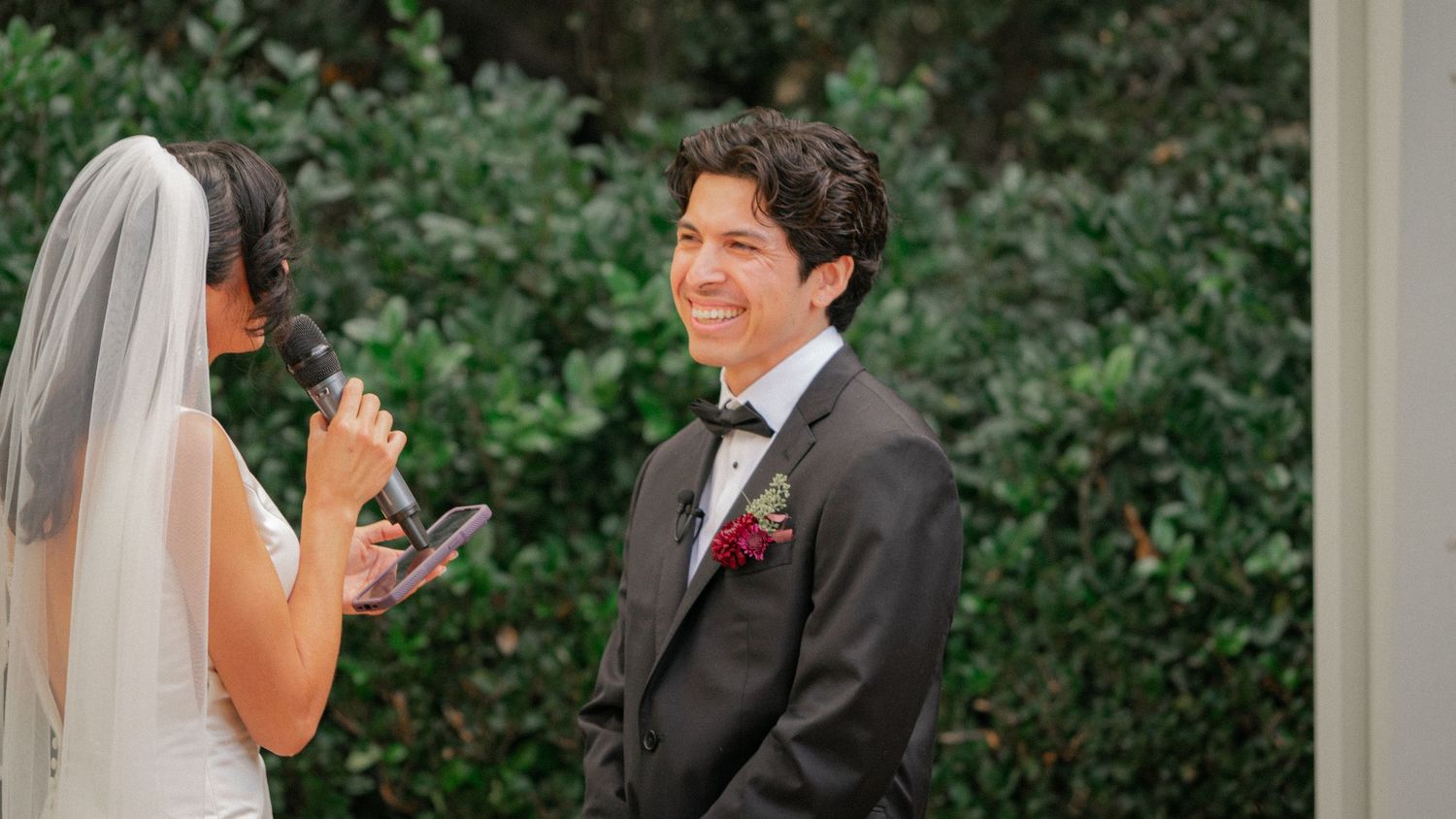 A wedding couple shares a candid moment together while walking outdoors among lush green foliage.