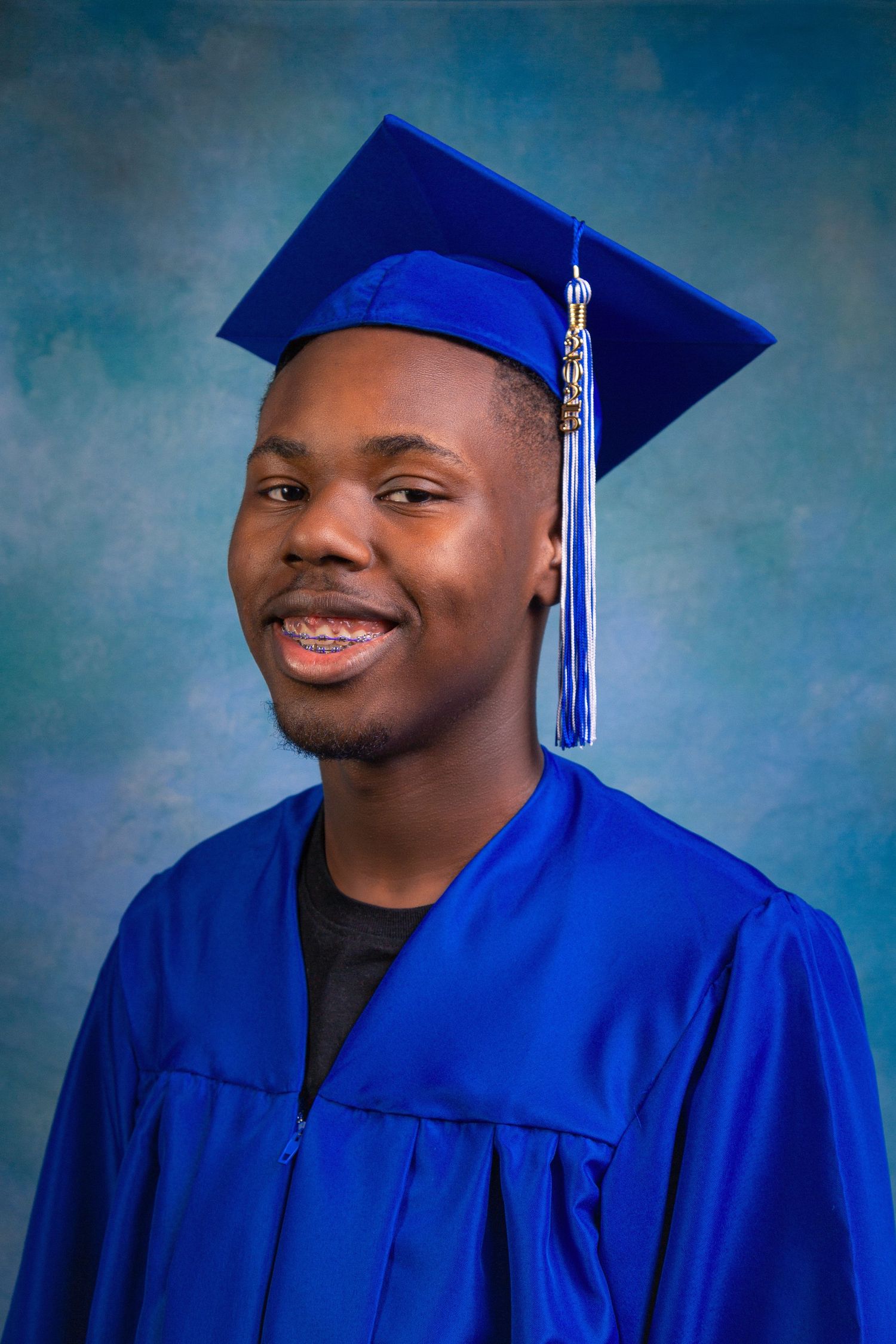 Graduate in royal blue cap and gown smiles warmly against blue backdrop in professional portrait series.