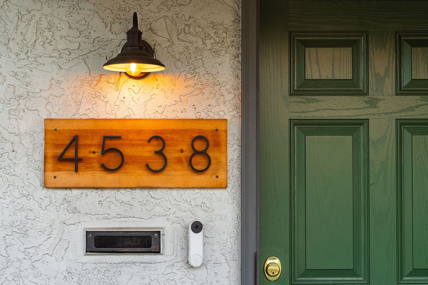 A series of green doors and textured walls with house numbers illuminated by warm lighting in a residential hallway.
