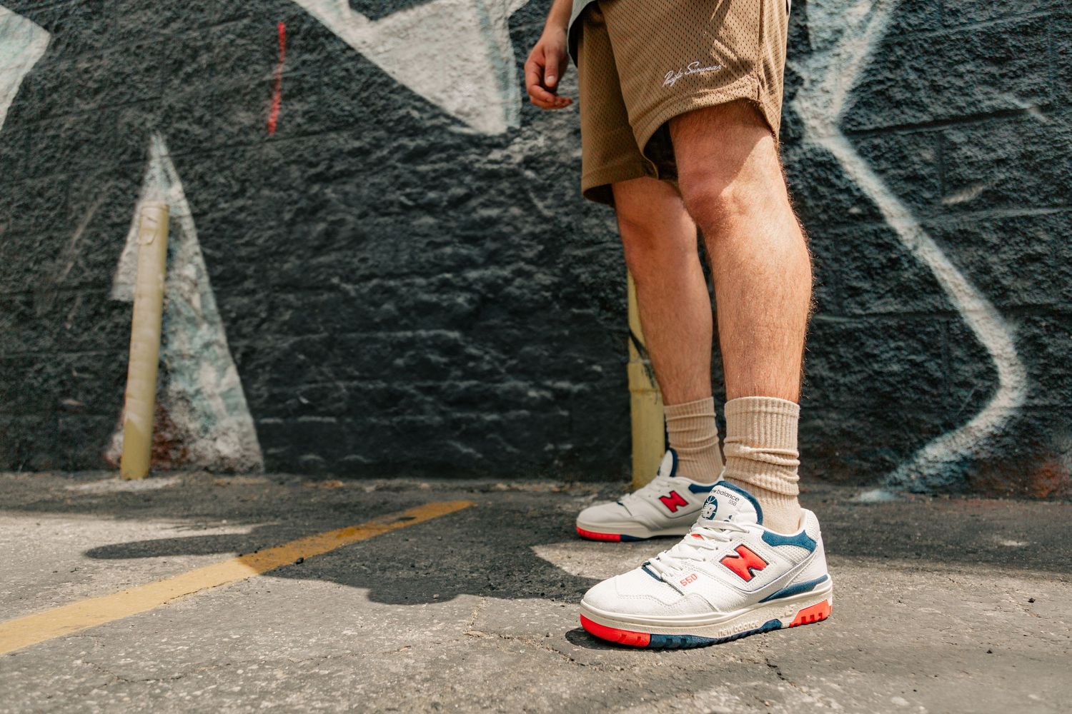 Low angle view of legs wearing white and red Nike sneakers against a black graffiti wall background.