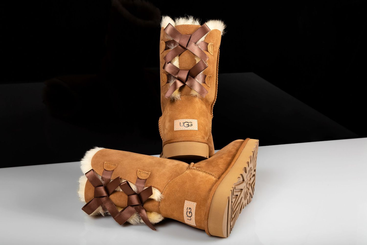 A pair of tan UGG boots with bows on the back shown from multiple angles against a dark background.