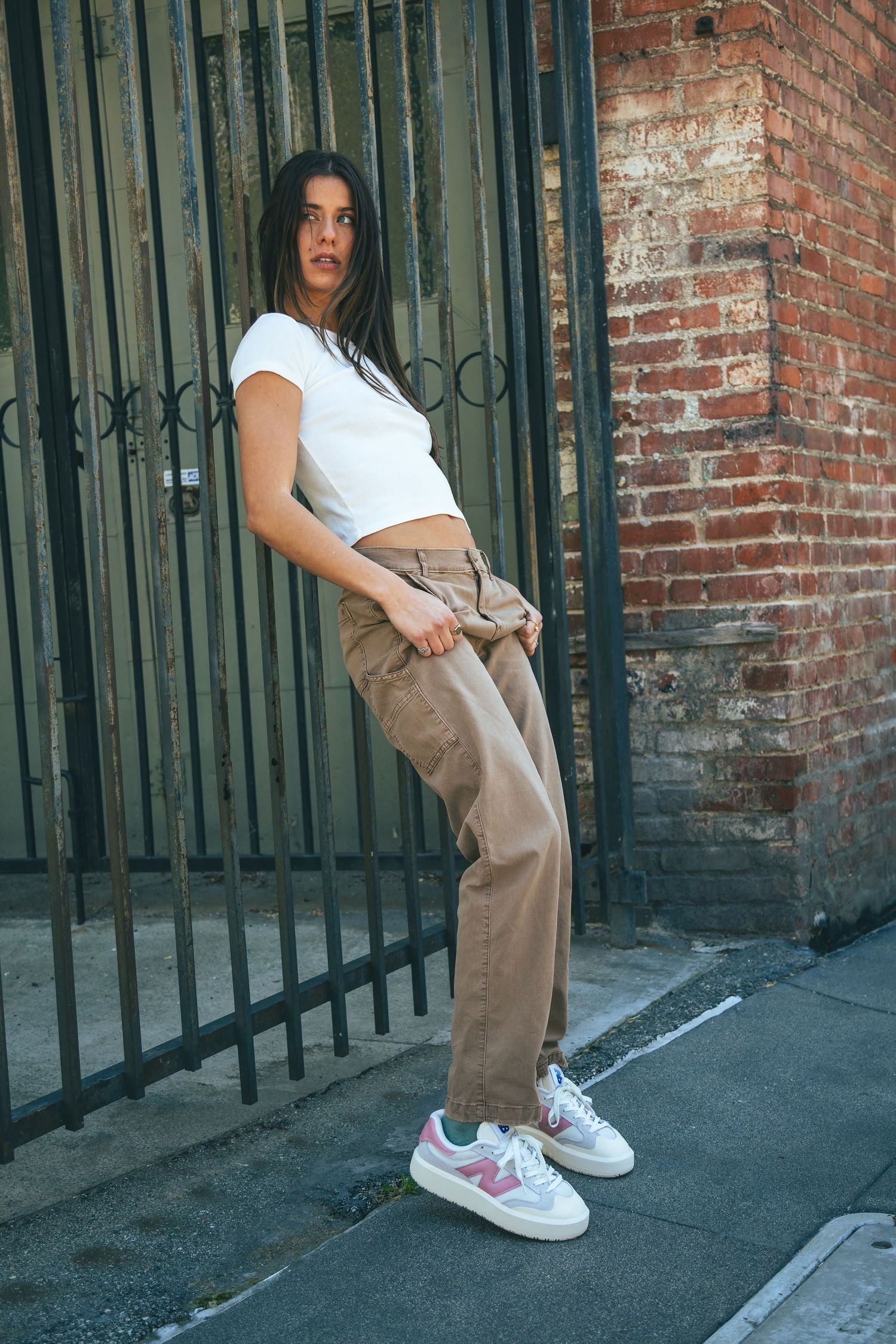 Four connected photos showing someone in a white crop top and khaki pants posing against a brick wall with iron gates.