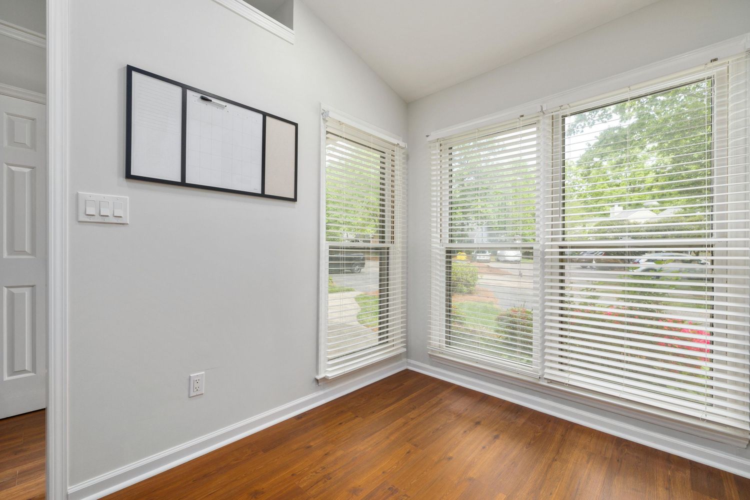 Modern white living room with large windows, grey walls, and hardwood floors in an open concept layout.