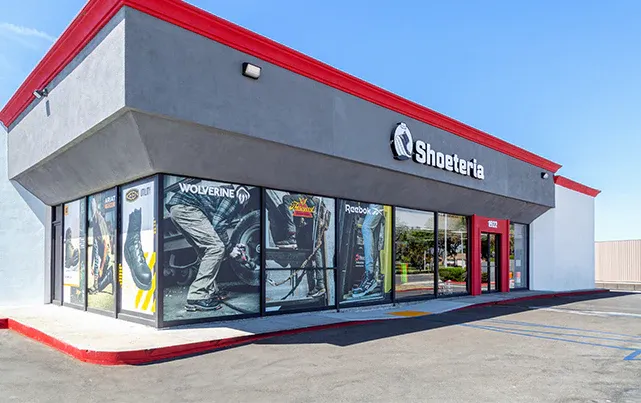 Modern commercial retail strip mall exterior with red accent trim and glass storefronts on a sunny day.