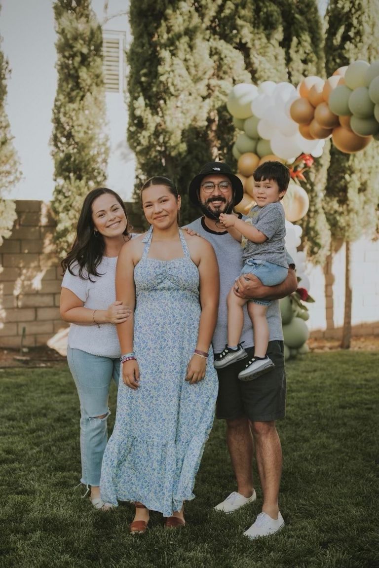 Family members in matching blue floral dresses share joyful moments together on a grassy lawn at sunset.