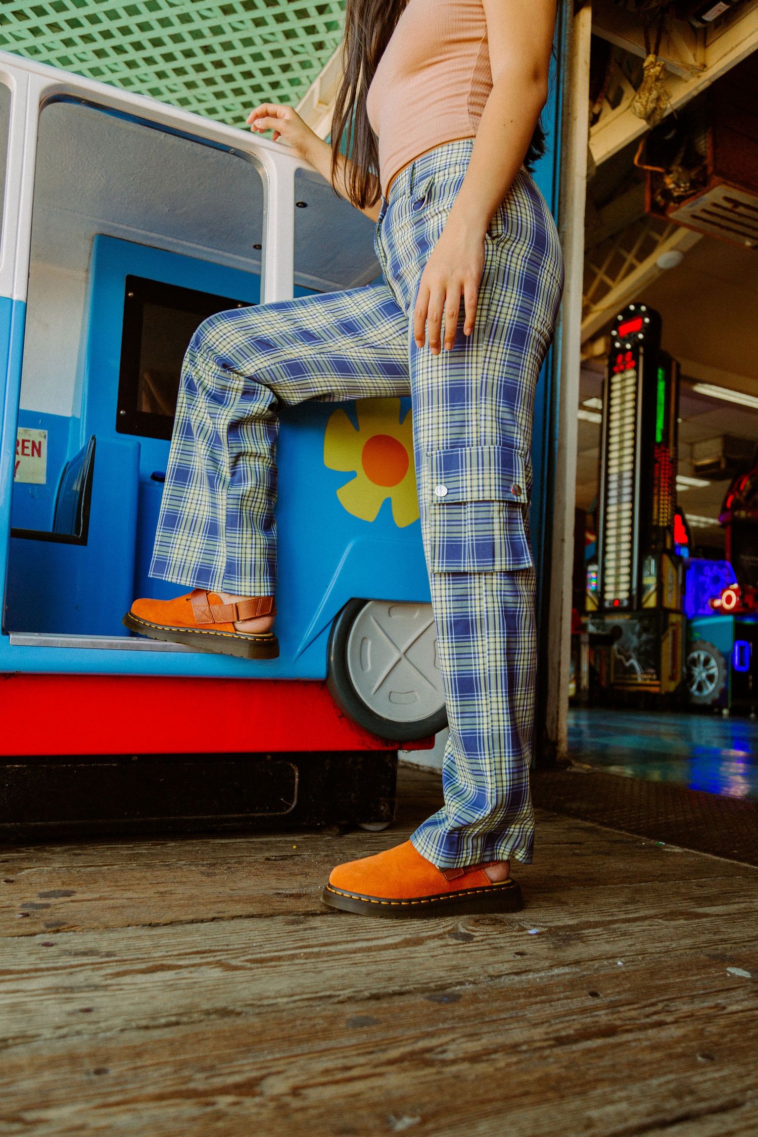 Retro plaid pants and orange loafers shown against a blue vintage van with flower decal on wooden floor.