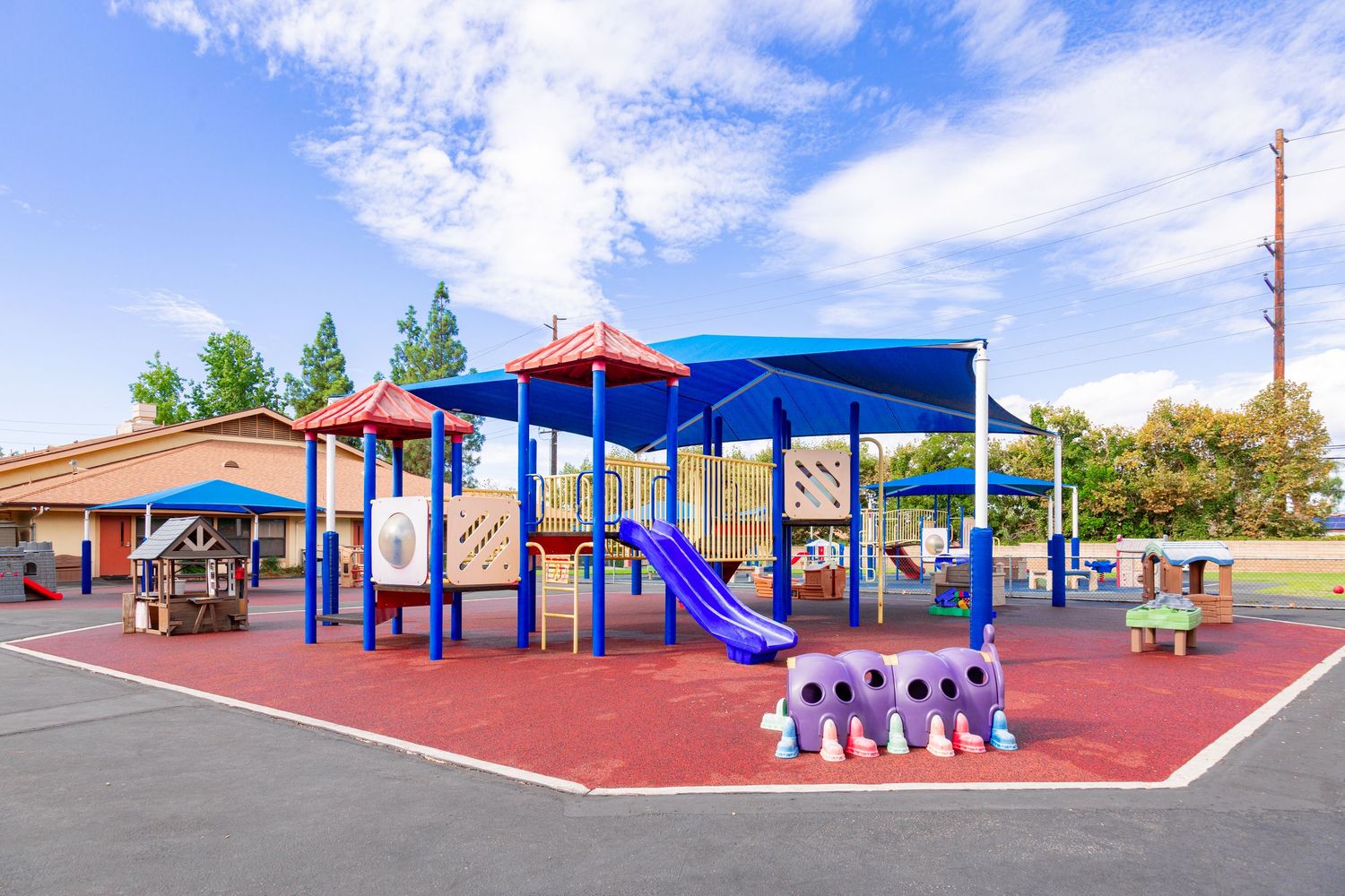 A modern playground with colorful equipment and rubber safety surfacing features multiple play structures under a blue sky.