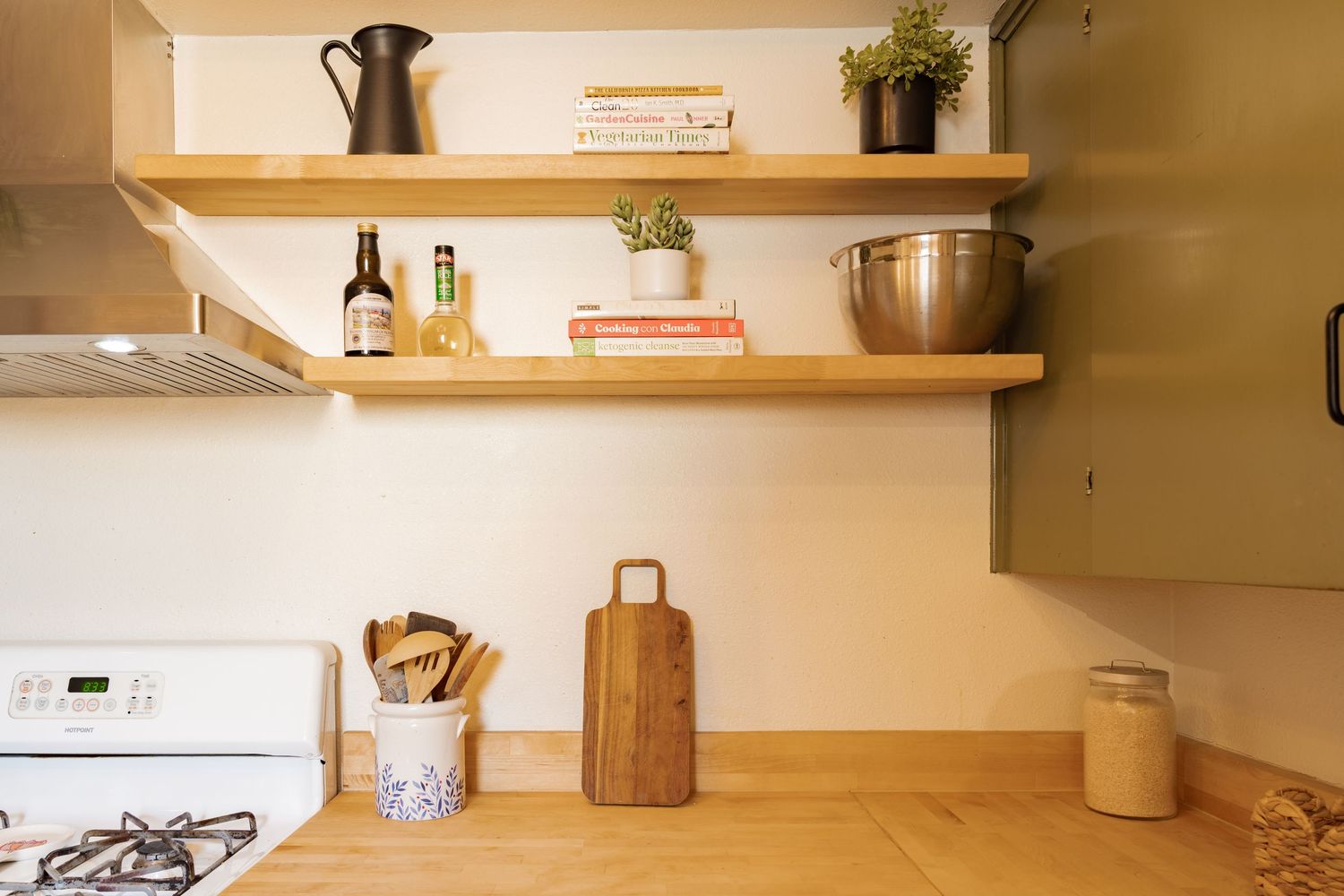 Modern kitchen interior with wooden floating shelves displaying cookware and decor against a warm-toned wall.