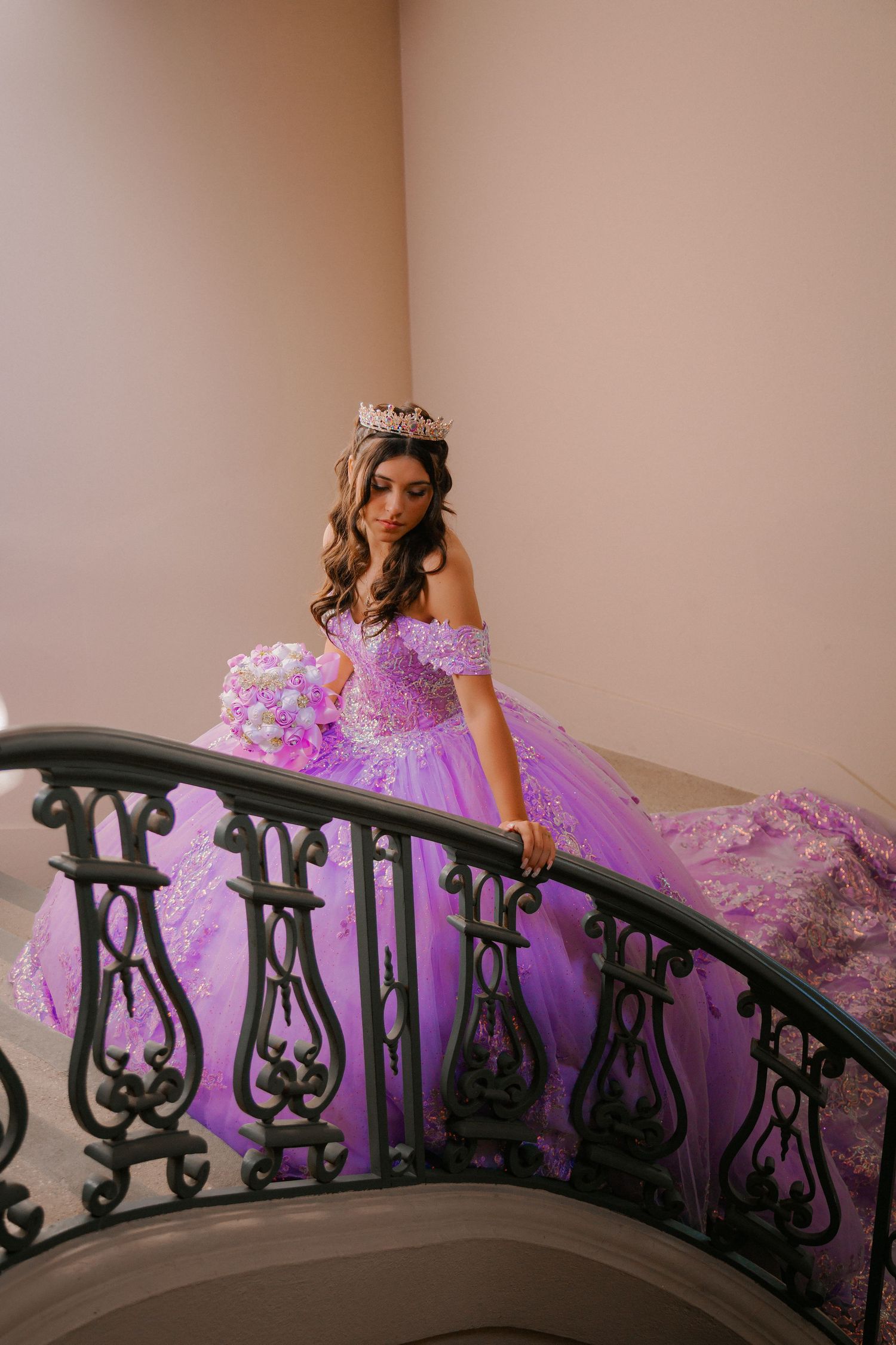 A figure in a flowing lavender ballgown poses gracefully along an ornate black iron staircase railing.