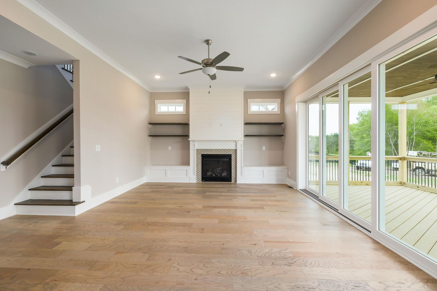 Modern open concept living room with light hardwood floors, white walls, and large windows overlooking a deck.