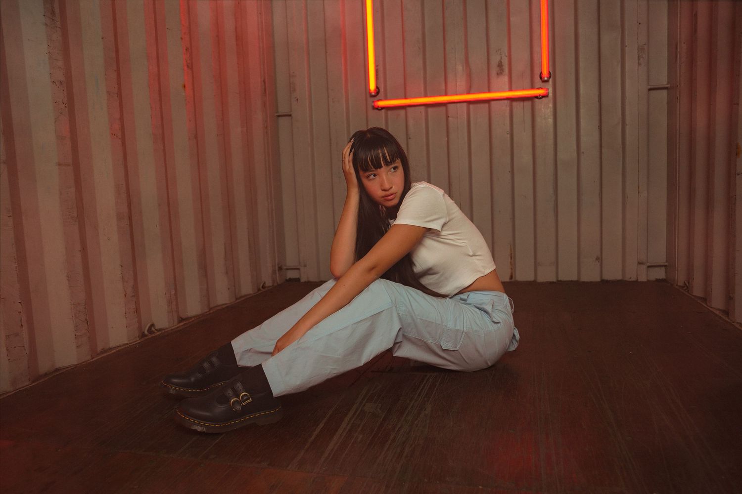 A person in white clothing poses on a metallic surface with dramatic red lighting creating a moody atmosphere.