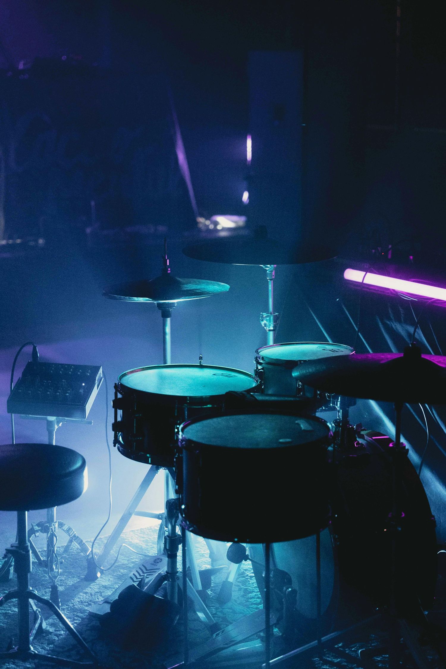 A dark atmospheric shot of a drum kit silhouetted by blue and purple lighting on a foggy stage.