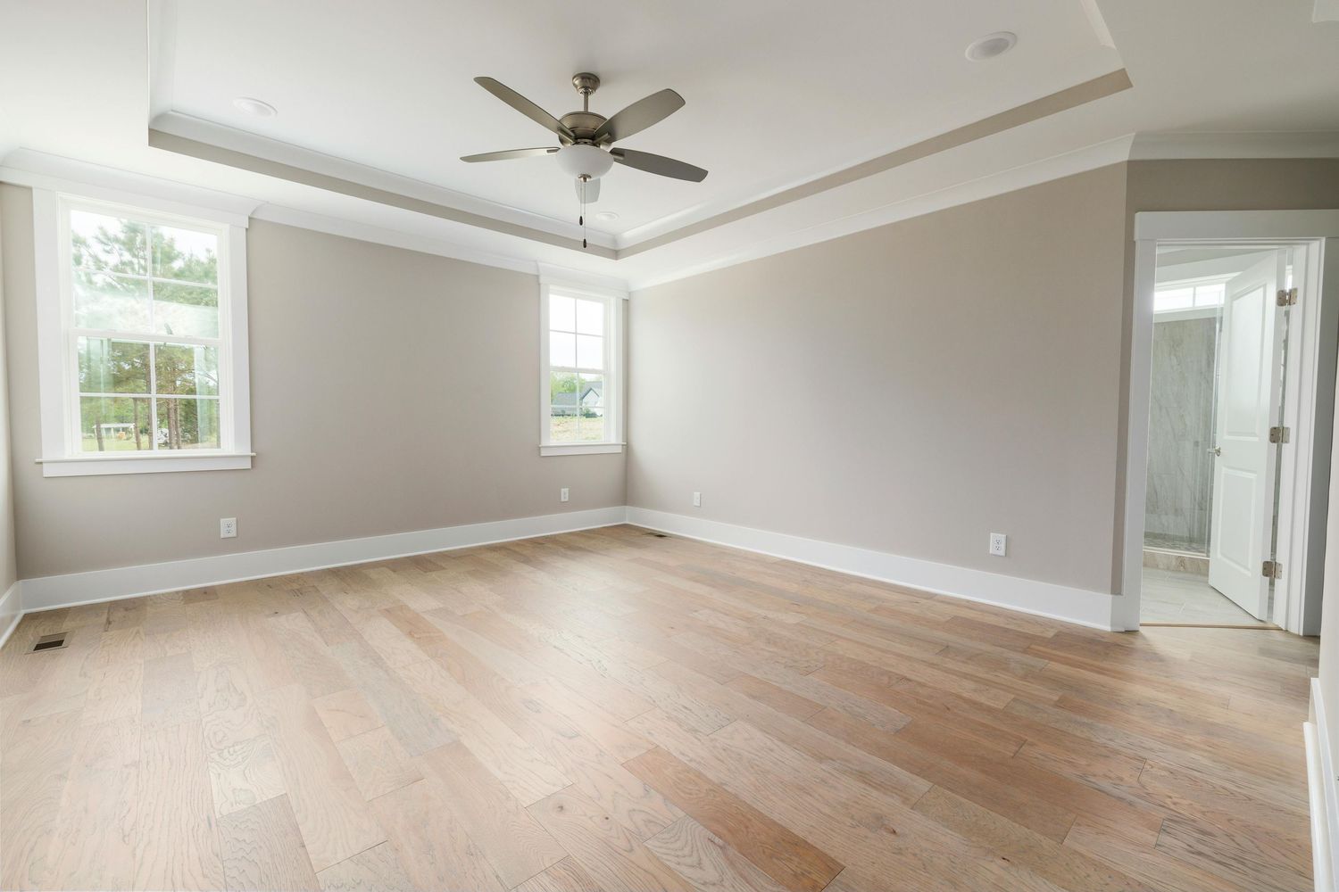 Modern empty bedroom with ceiling fan, recessed lighting, and hardwood floors showcases bright neutral walls and windows.