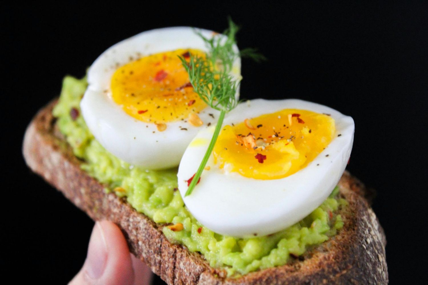 Slices of avocado toast with perfectly cooked soft boiled eggs and fresh herbs on dark bread.