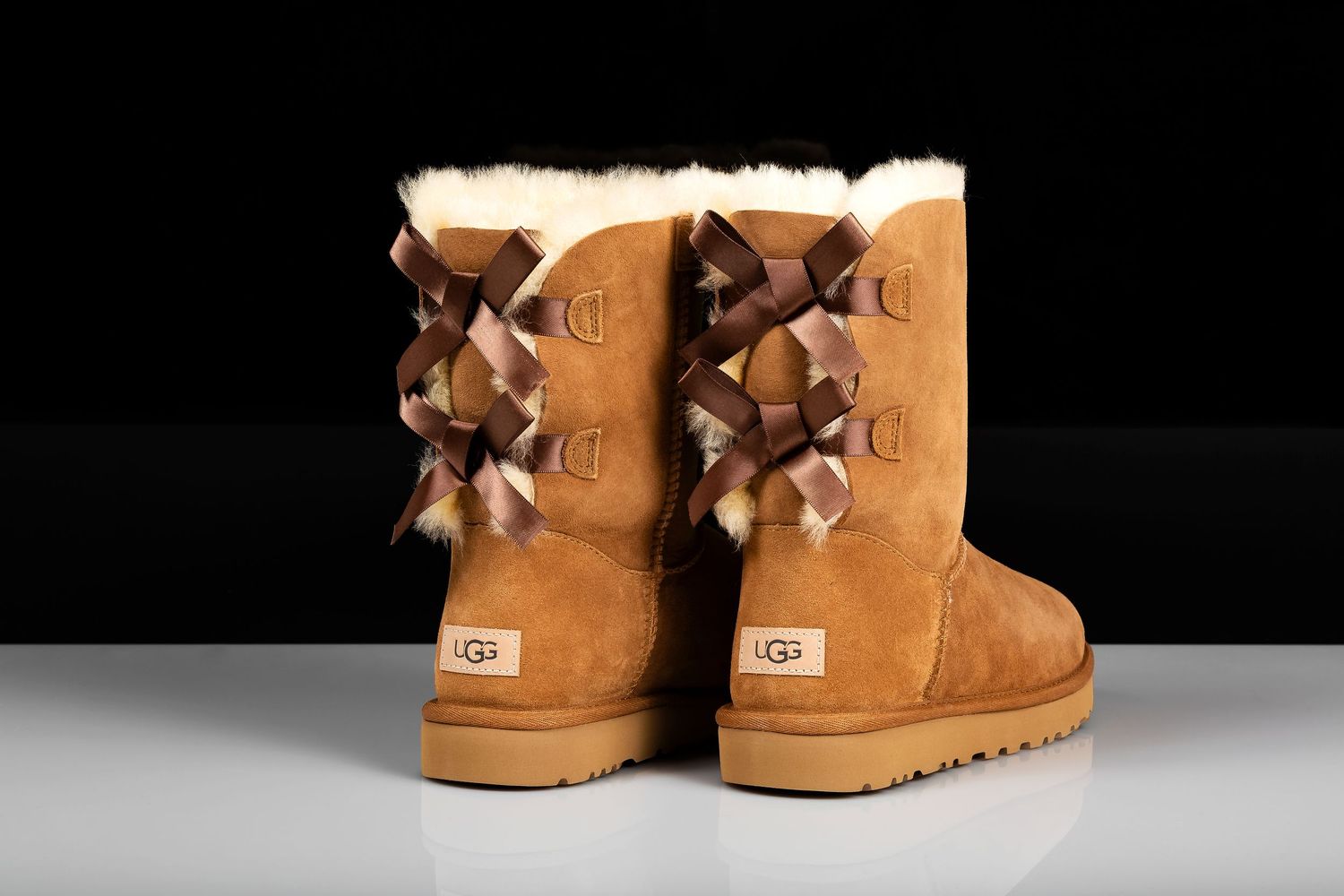 Tan suede UGG boots with decorative bow details shown from multiple angles on dark background.
