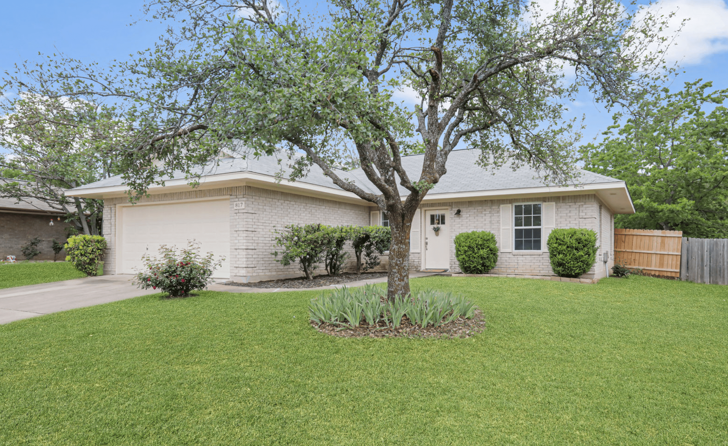Single-story white ranch house with attached garage and well-maintained front lawn featuring mature trees and landscaping.
