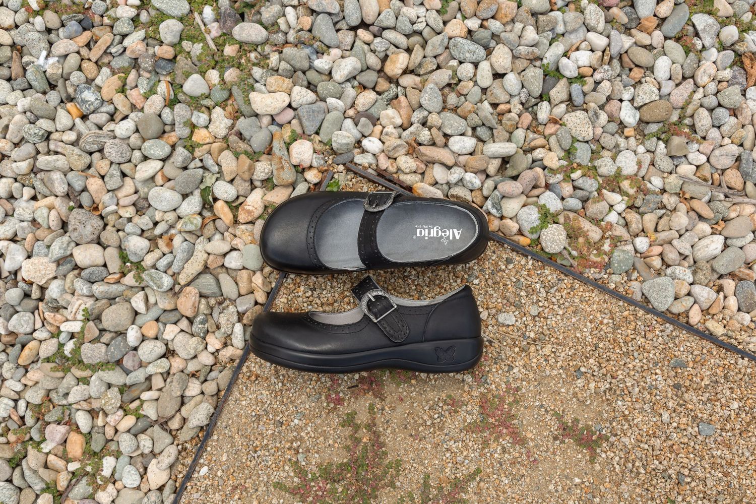 A black leather shoe sits on a pebbled surface showing different angles and perspectives of the footwear.