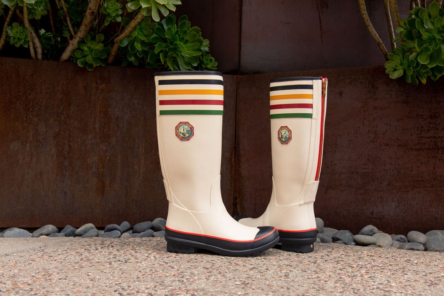 White cowboy boots with colorful striped accents sit on a speckled floor against a dark wooden wall.