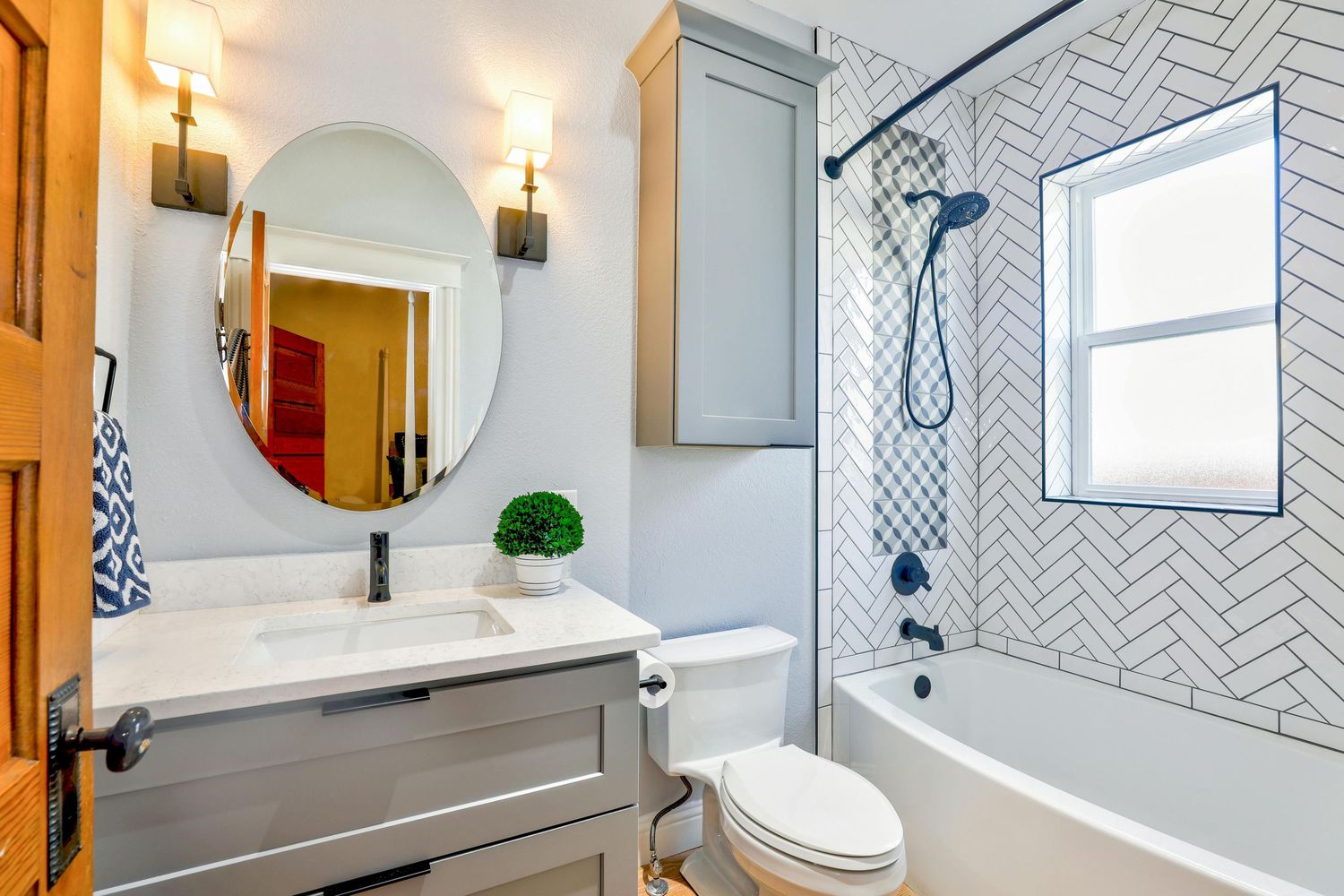 A modern bathroom features white herringbone tile walls, blue accents, and a circular mirror above the vanity.