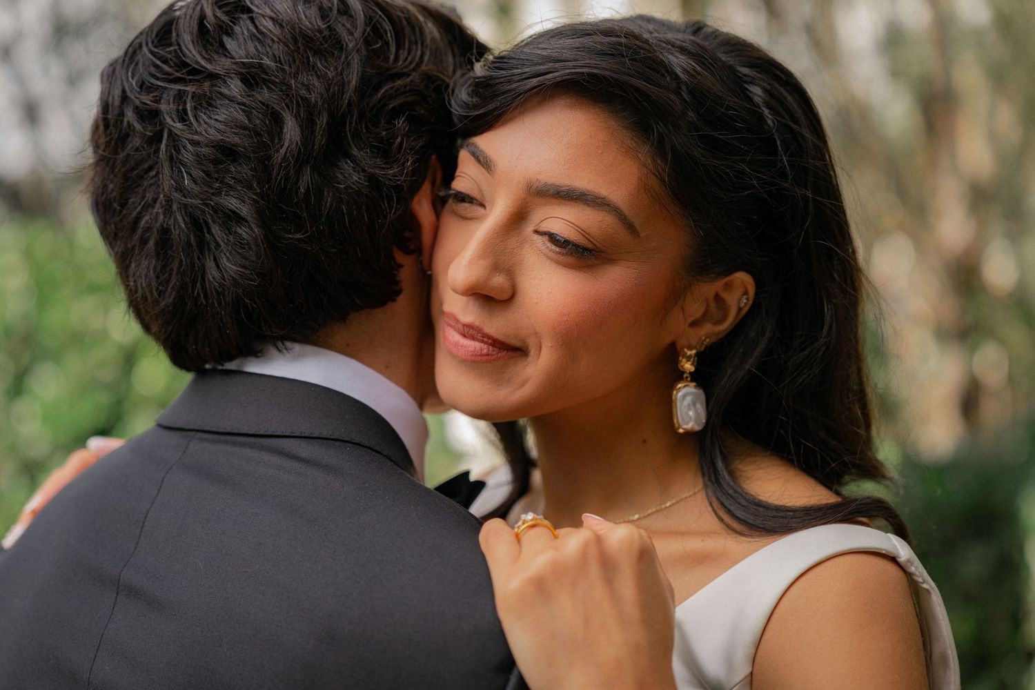A romantic couple embraces outdoors during a wedding photoshoot in a lush garden setting.