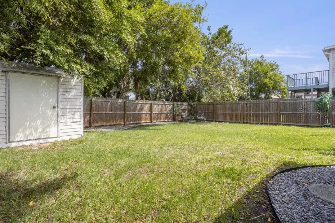 Fenced backyard with green grass lawn, white garage, and mature trees providing natural shade.