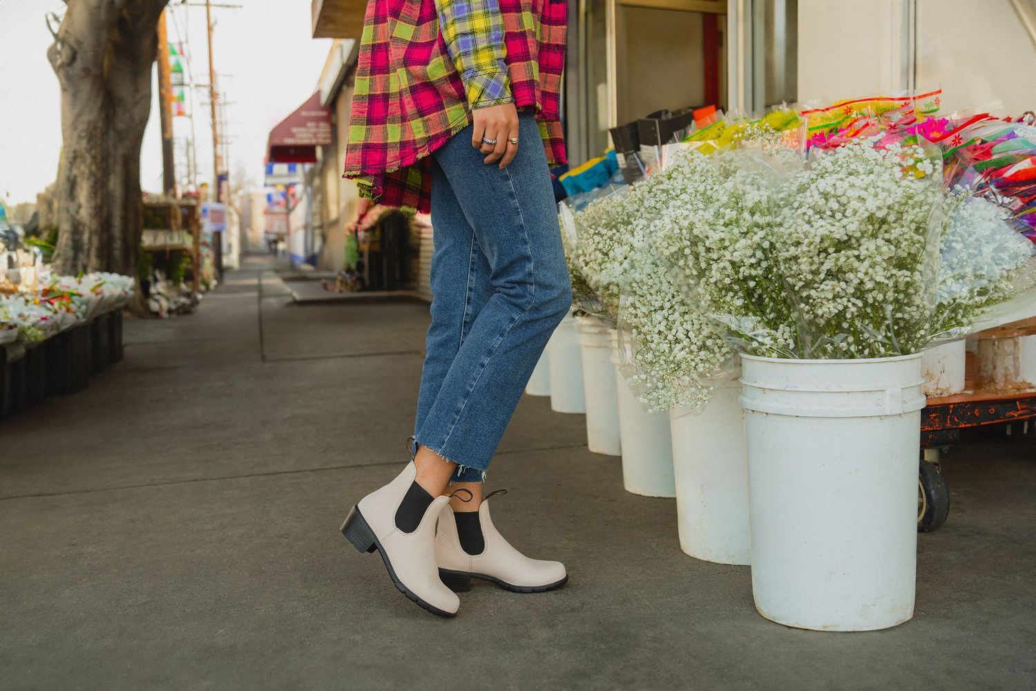 People walking past white flower displays at an outdoor market or street fair.