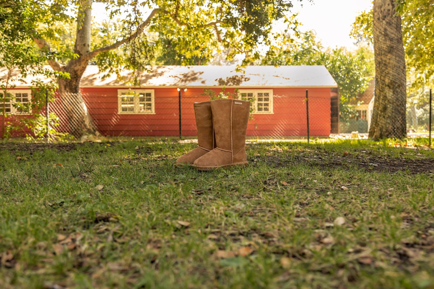 A red wooden barn building sits on a grassy lawn surrounded by autumn trees with golden leaves.