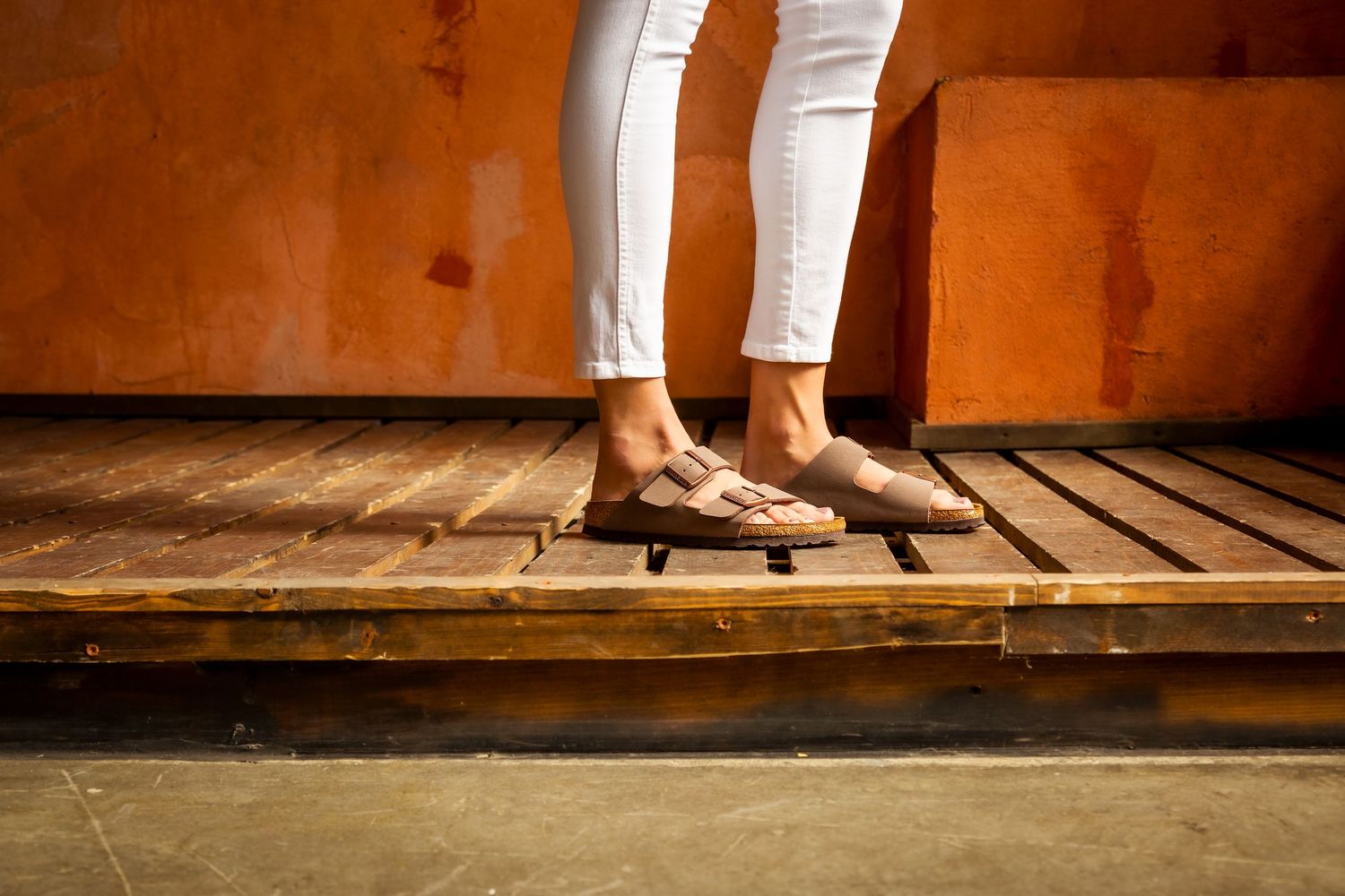 A person's feet in white sneakers walking across a wooden deck or boardwalk surface.