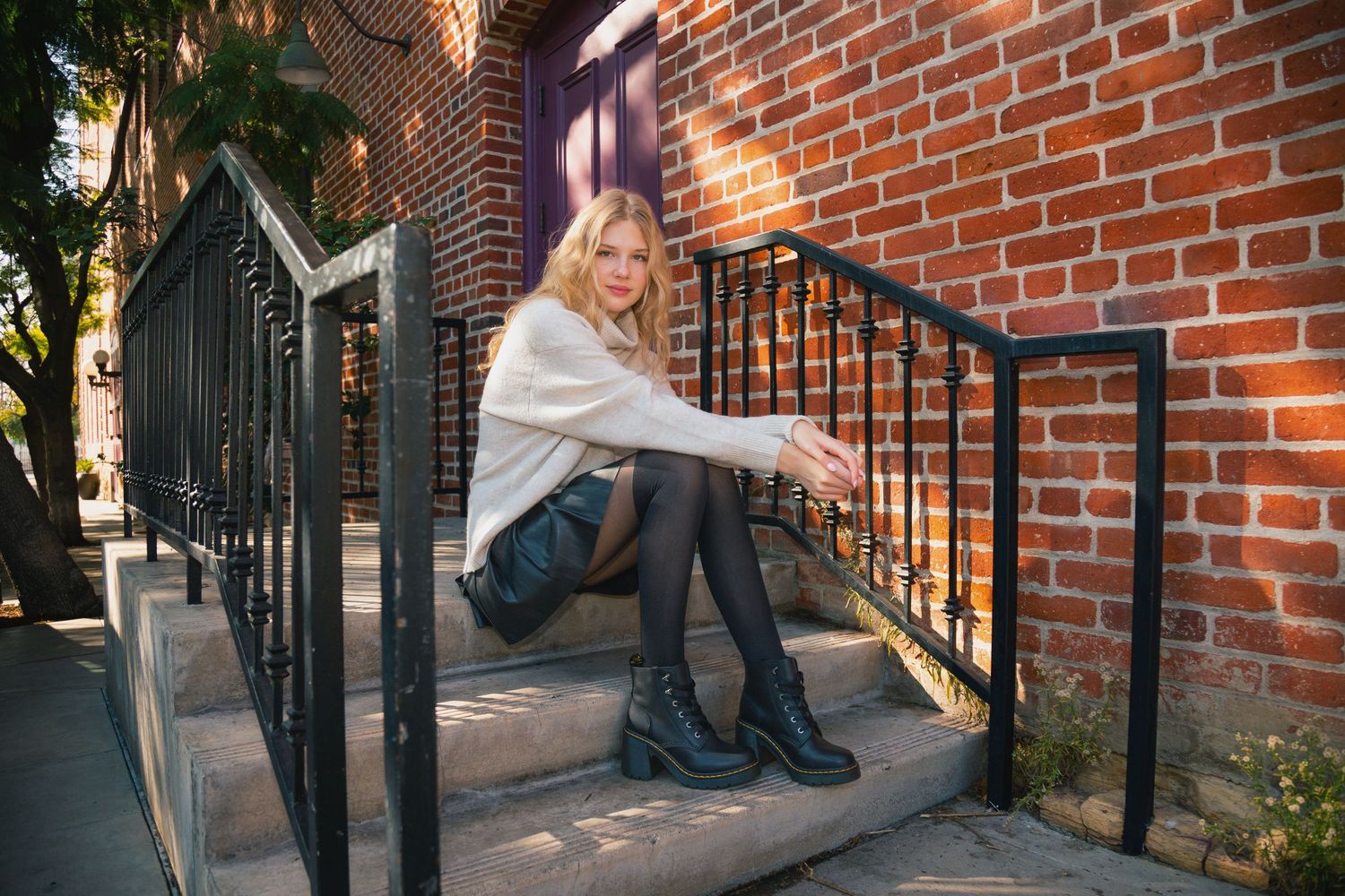 A person in jeans sits on brick steps while demonstrating different casual poses against a brick wall.