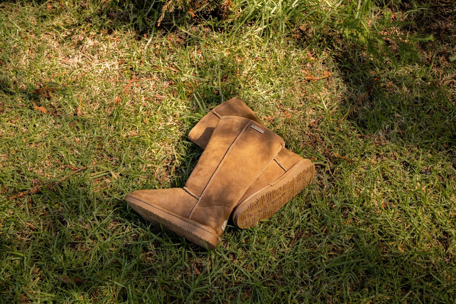 Brown leather work boots sit scattered on green grass in sunlight showing wear and patina from regular use.