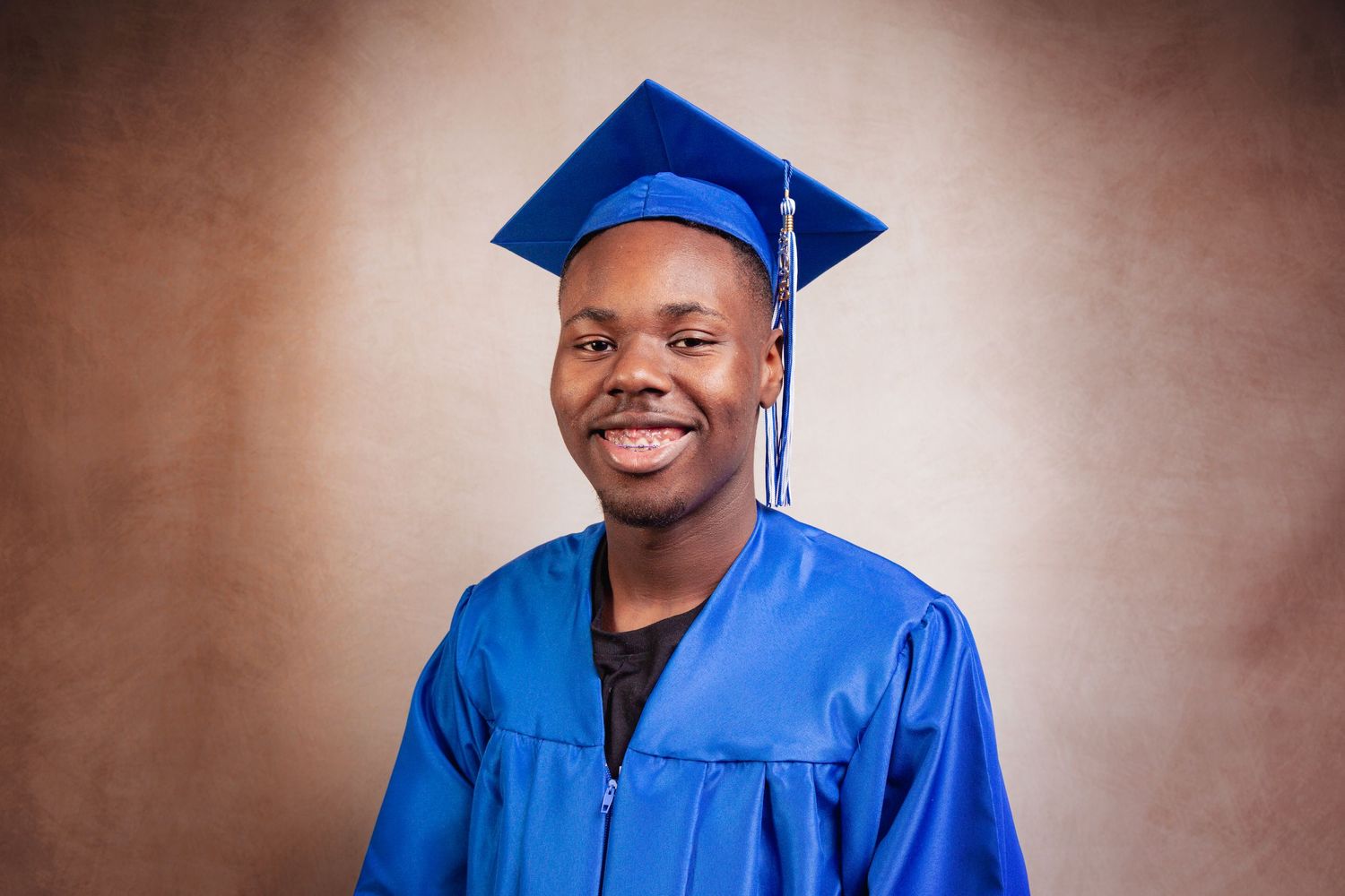 Graduate in blue cap and gown poses for a series of celebratory portraits against a brown backdrop.