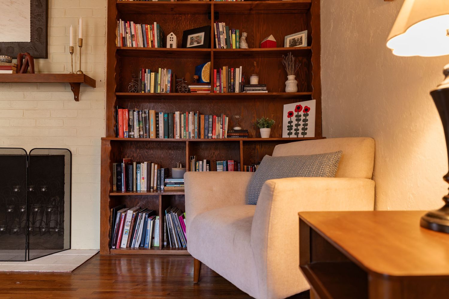 A cozy home library corner with wooden shelves filled with books, illuminated by a warm table lamp.