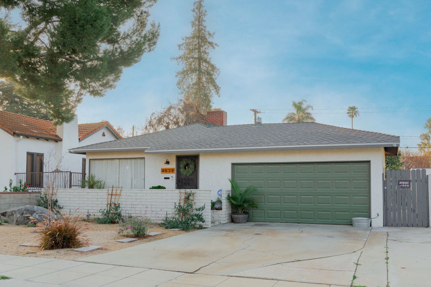 Single-story ranch house with white exterior, green garage door and concrete driveway under blue sky.