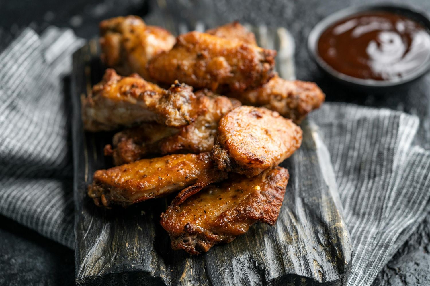 Crispy golden chicken wings with sauce served on a rustic wooden surface with a dark background.