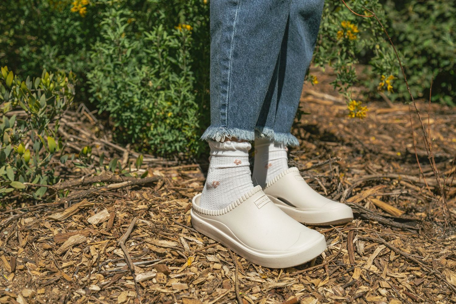 White sneakers walking on a dirt path with scattered leaves and grass visible in the outdoor setting.