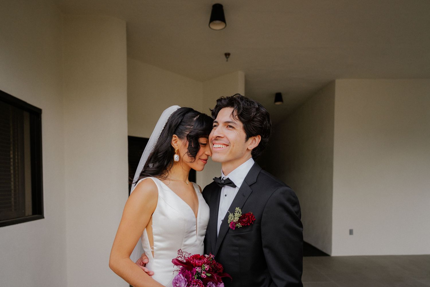 A couple shares a romantic kiss in a white hallway during their wedding celebration.