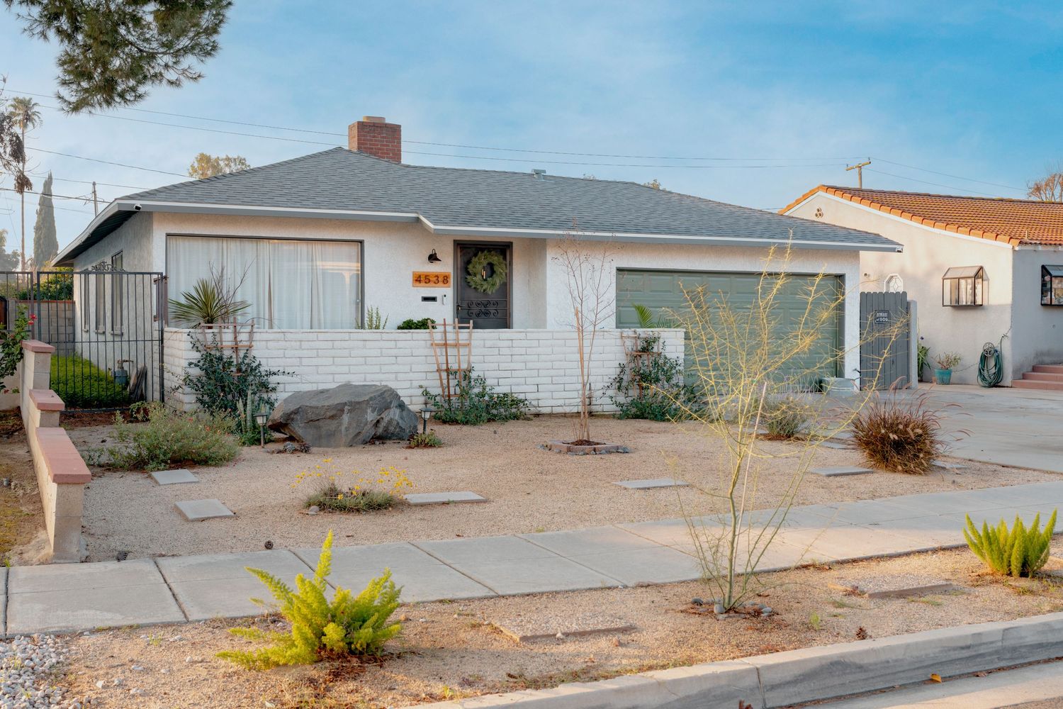 Single-story desert ranch house with white exterior and attached garage on a sloped lot under bright blue sky.