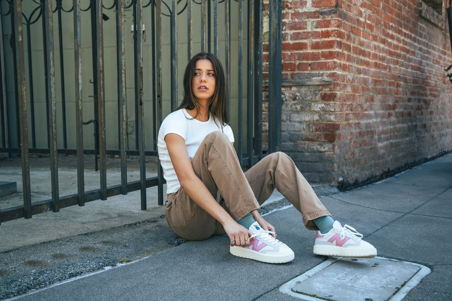 A person in casual white shirt and khaki pants sits on concrete steps against a rustic brick wall.