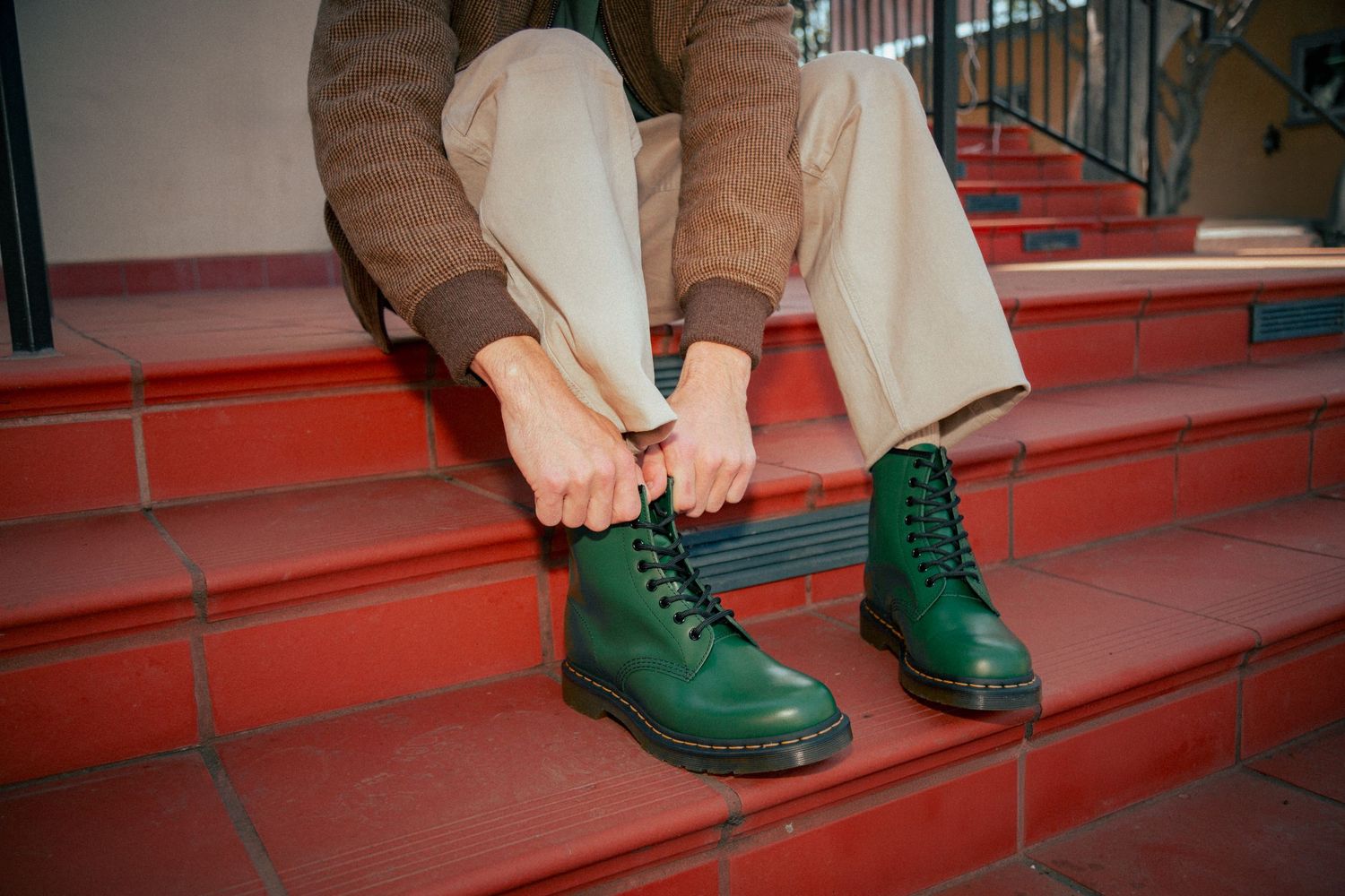 Close-up sequence showing green Dr. Martens boots being laced up on red brick steps.